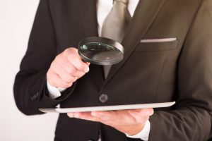 Businessman checking a tablet with magnifying glass